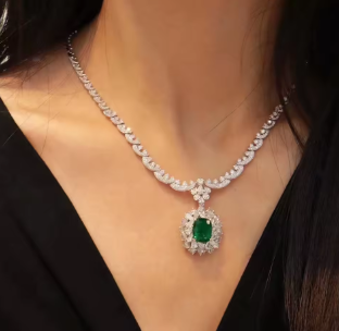 Close-up of a diamond necklace with a green gemstone on a person wearing a black top.